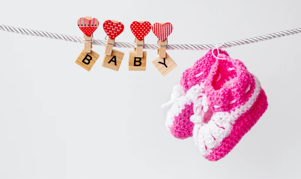 Pink baby girl shoes hanging from a rope, adorned with baby-themed decorative clips that illustrate pink color psychology and cultural femininity symbolism.