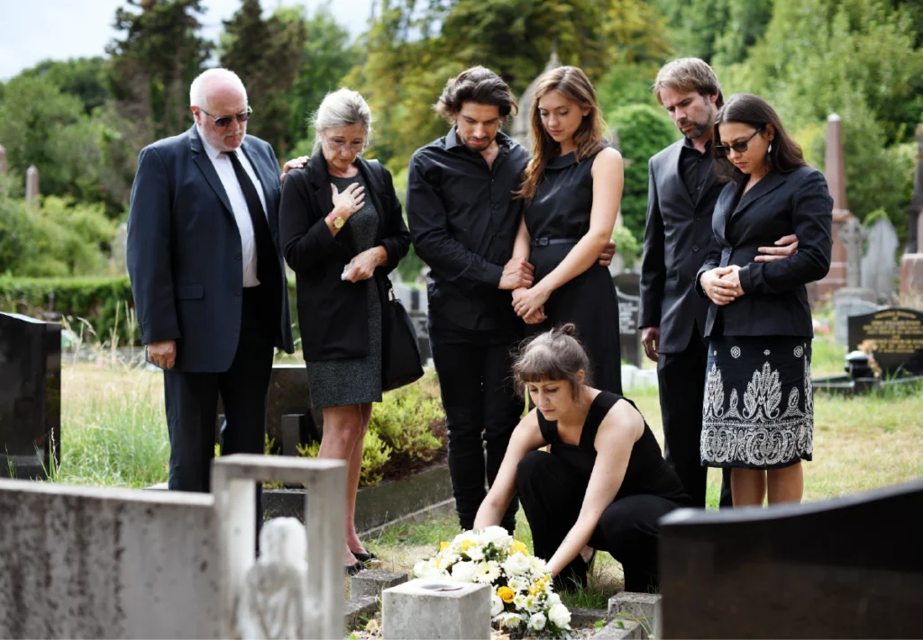 People dressed in black attending a graveside memorial, reflecting Western cultural associations between black and mourning.